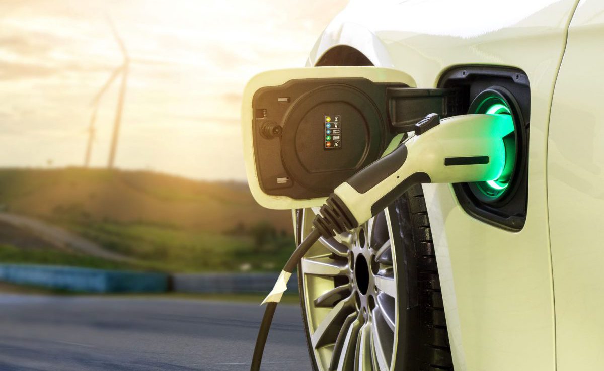 Electric car charging at a station with wind turbine in background.