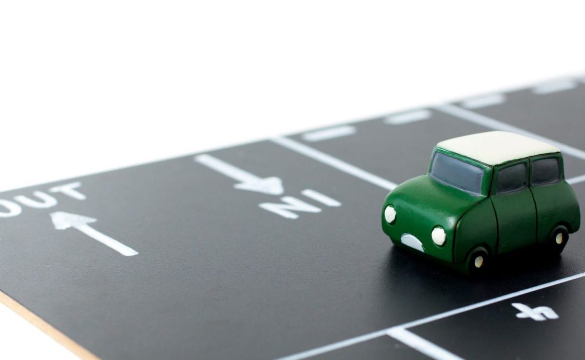 Miniature green toy car entering a marked parking bay, representing the shift from car ownership to flexible leasing options.