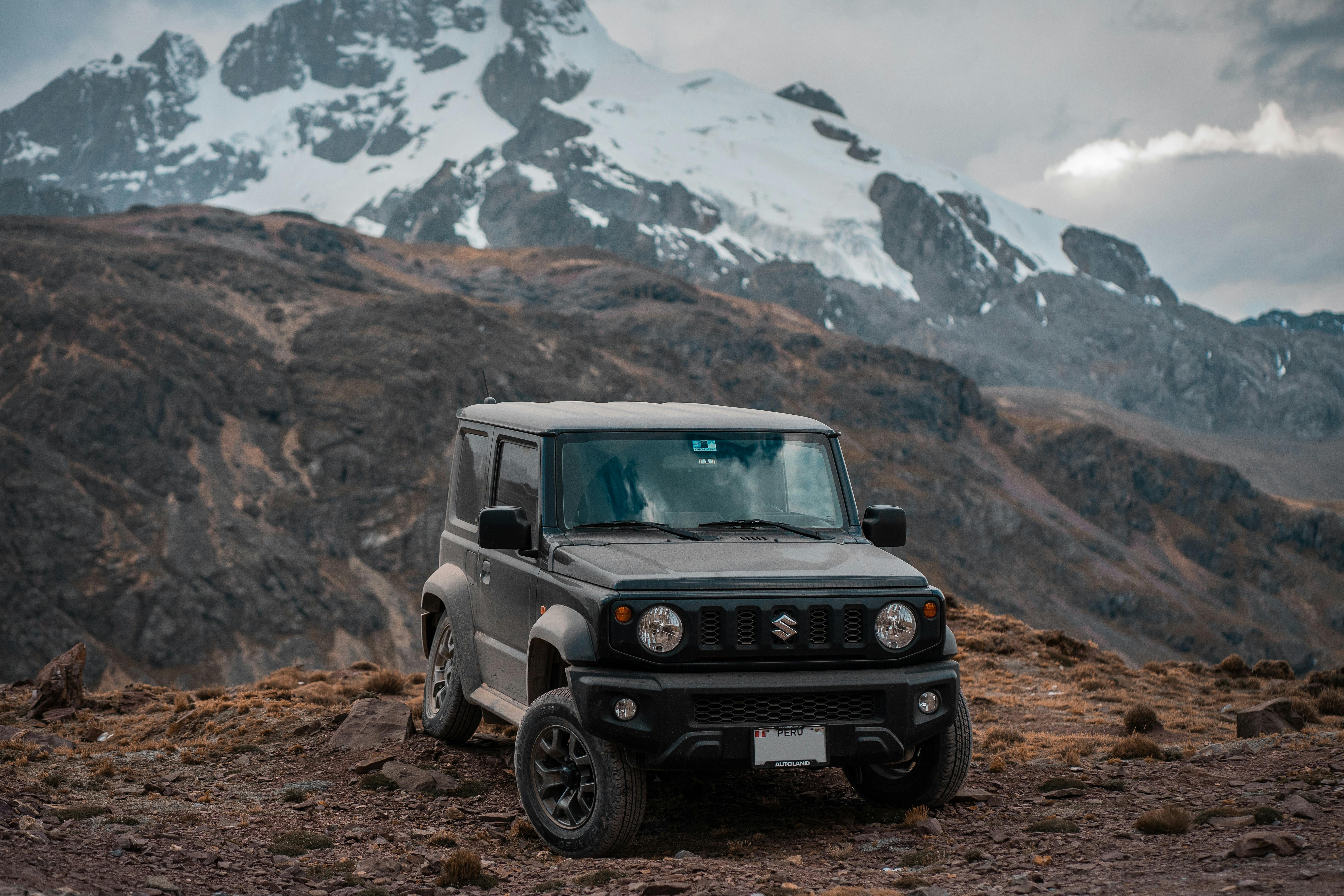 A Suzuki Jimny maneuvering through a dense, forested trail, showcasing its compact yet sturdy build and impressive off-road capabilities. The vehicle features a boxy design, high ground clearance, and durable tyres, making it perfect for navigating tight spaces and challenging terrains with ease.