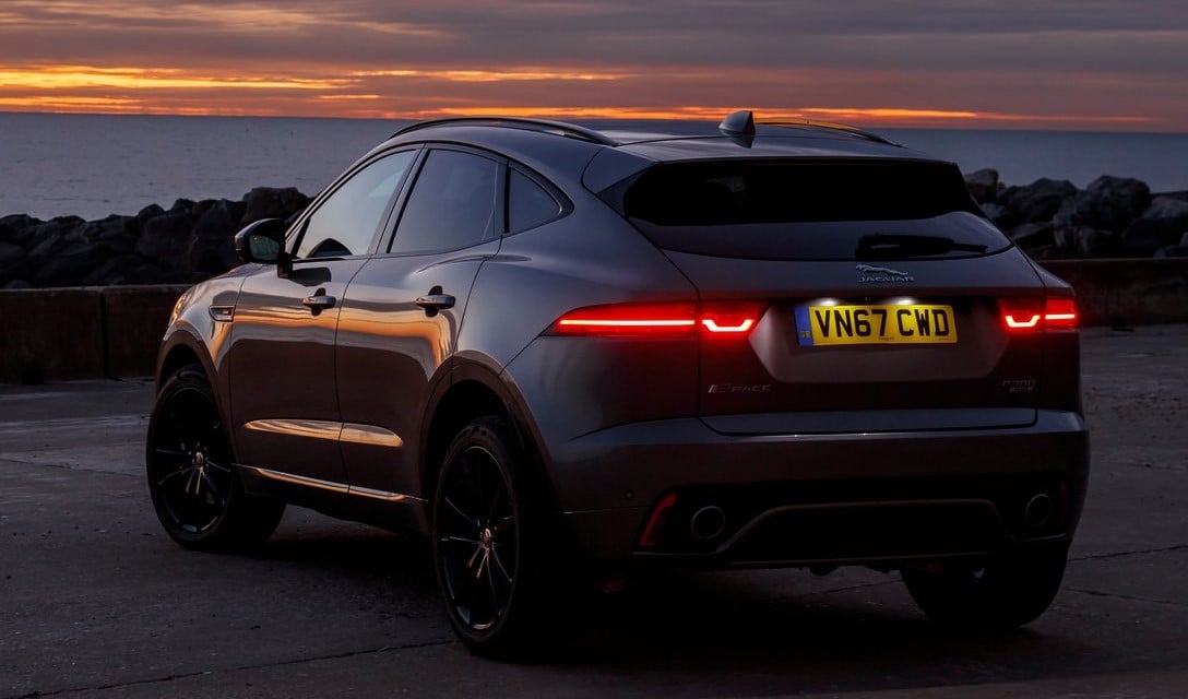 Rear view of a Jaguar E-Pace SUV parked at sunset near the coast, showcasing its sleek silhouette and LED tail lights.