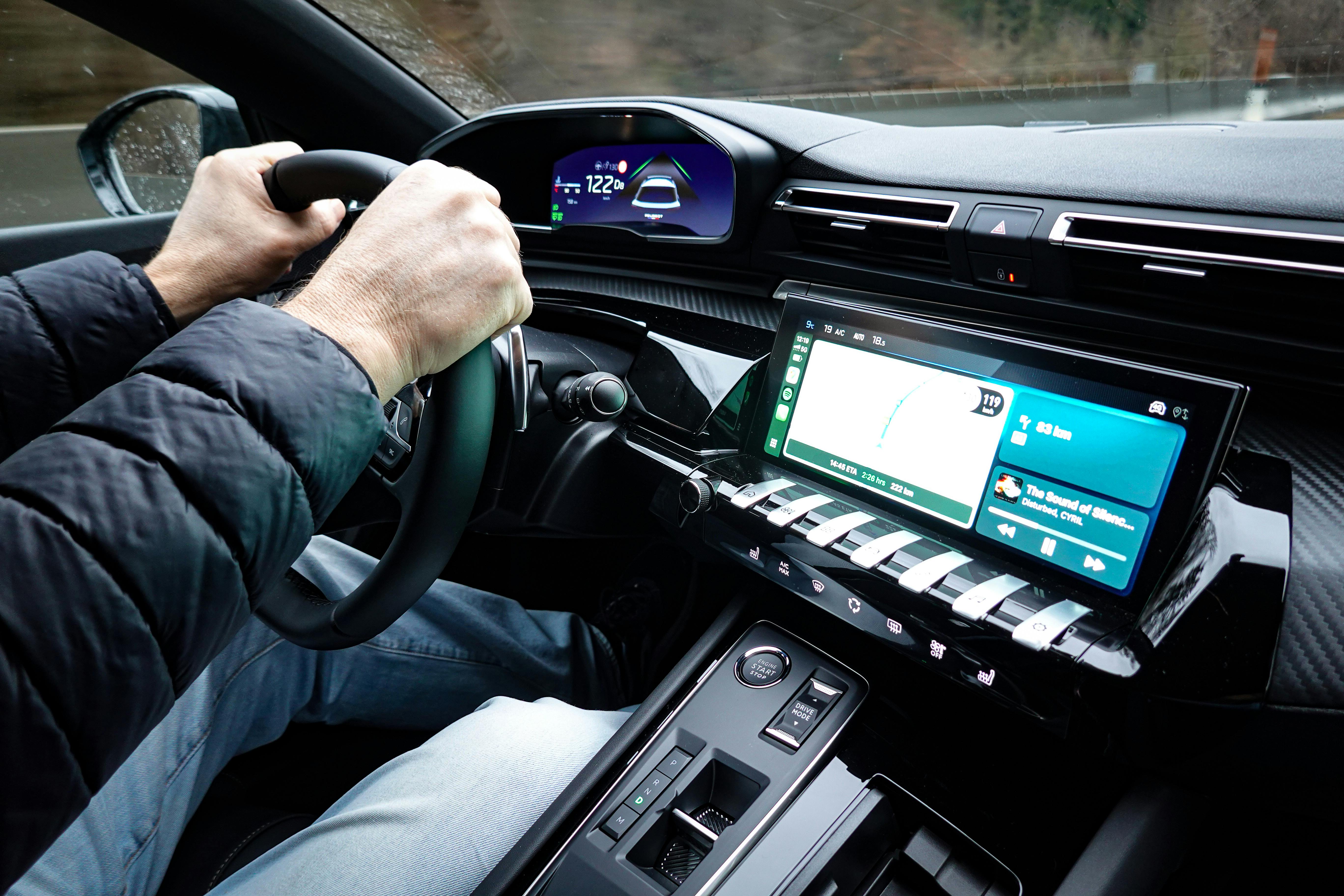 Driver holding the steering wheel of a modern car with a digital dashboard and navigation system on the display screen.