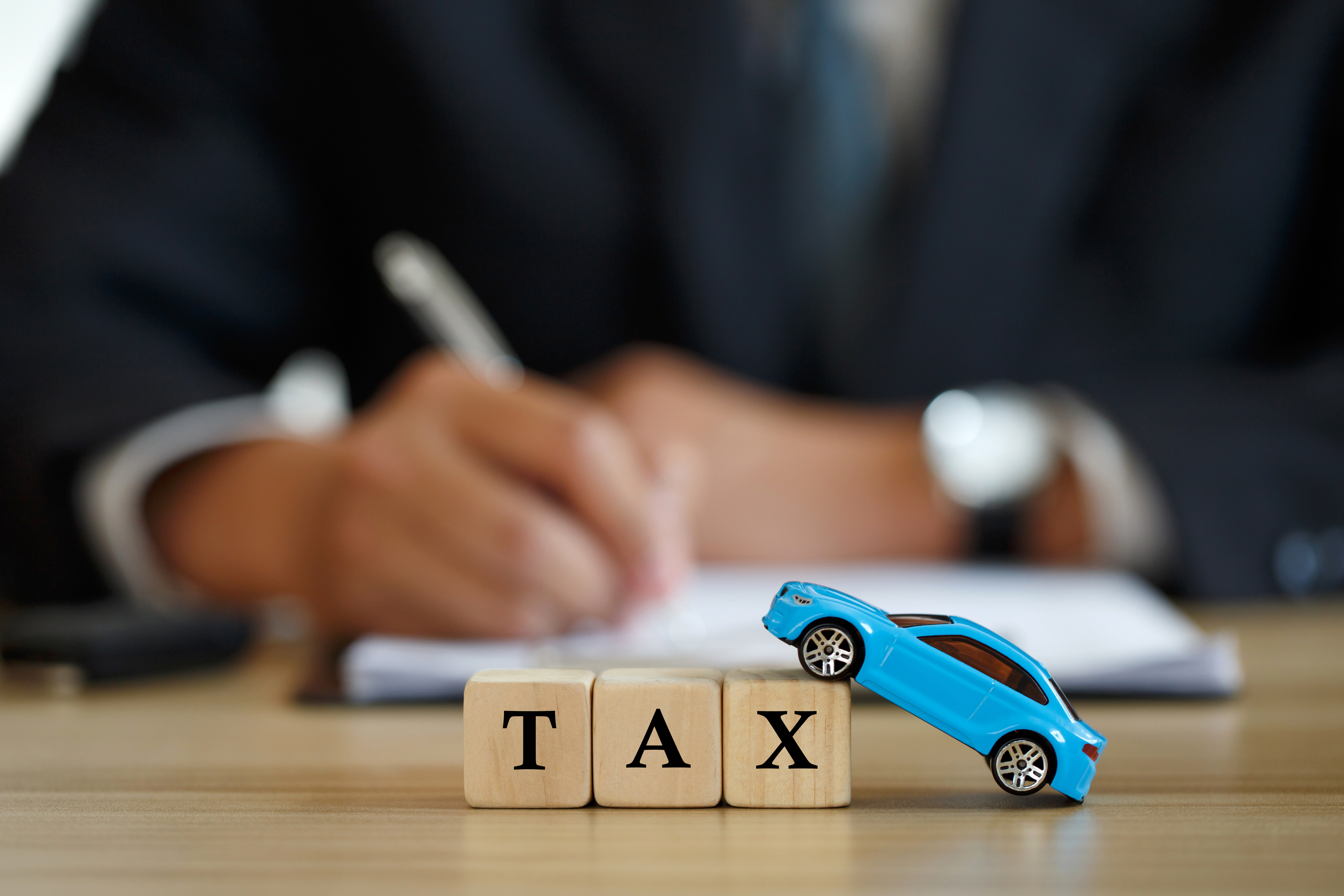 Person filling forms with tax blocks and car in-front of them