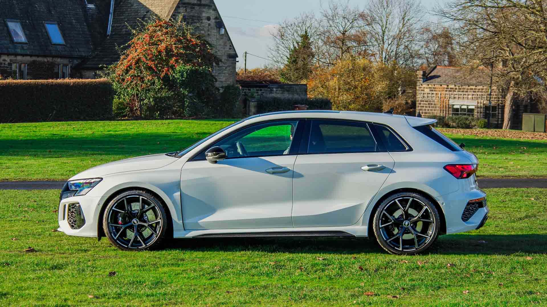 White Audi RS3 parked on grass, showcasing its sporty design, large alloy wheels, and aggressive styling for lease deals.