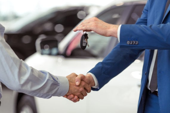 Two people shaking hands while exchanging car keys at a dealership, illustrating finance lease vs contract hire agreements.