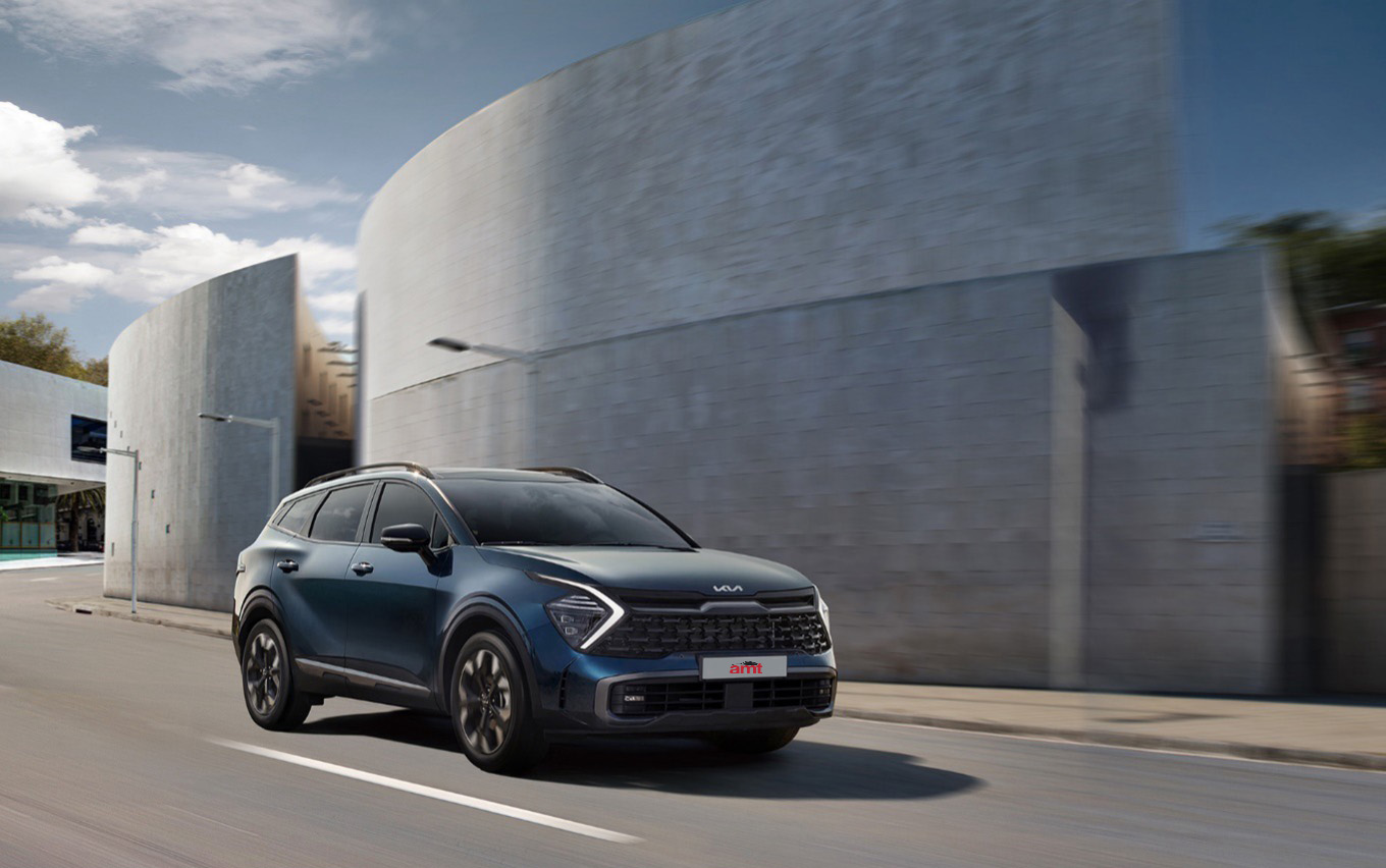 Kia Sportage driving through a modern urban setting, showcasing its bold SUV design and sleek front profile.