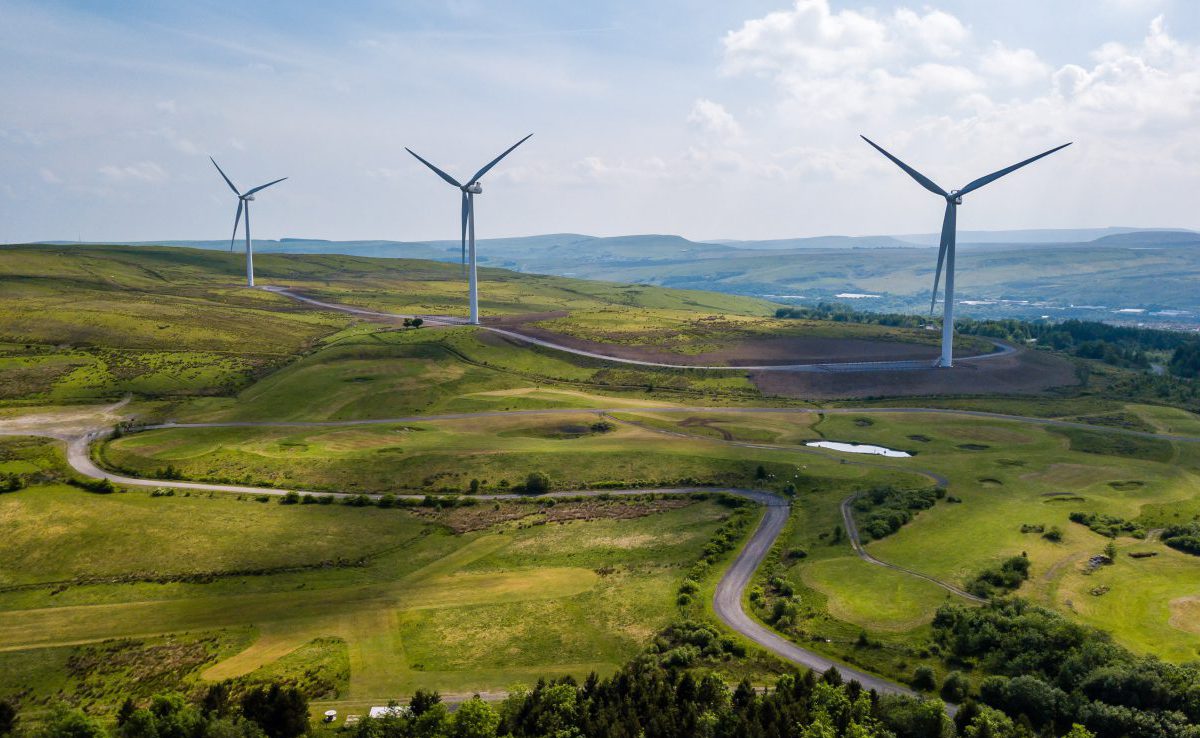 Wind turbines generating renewable energy on a green hillside under a partly cloudy sky.