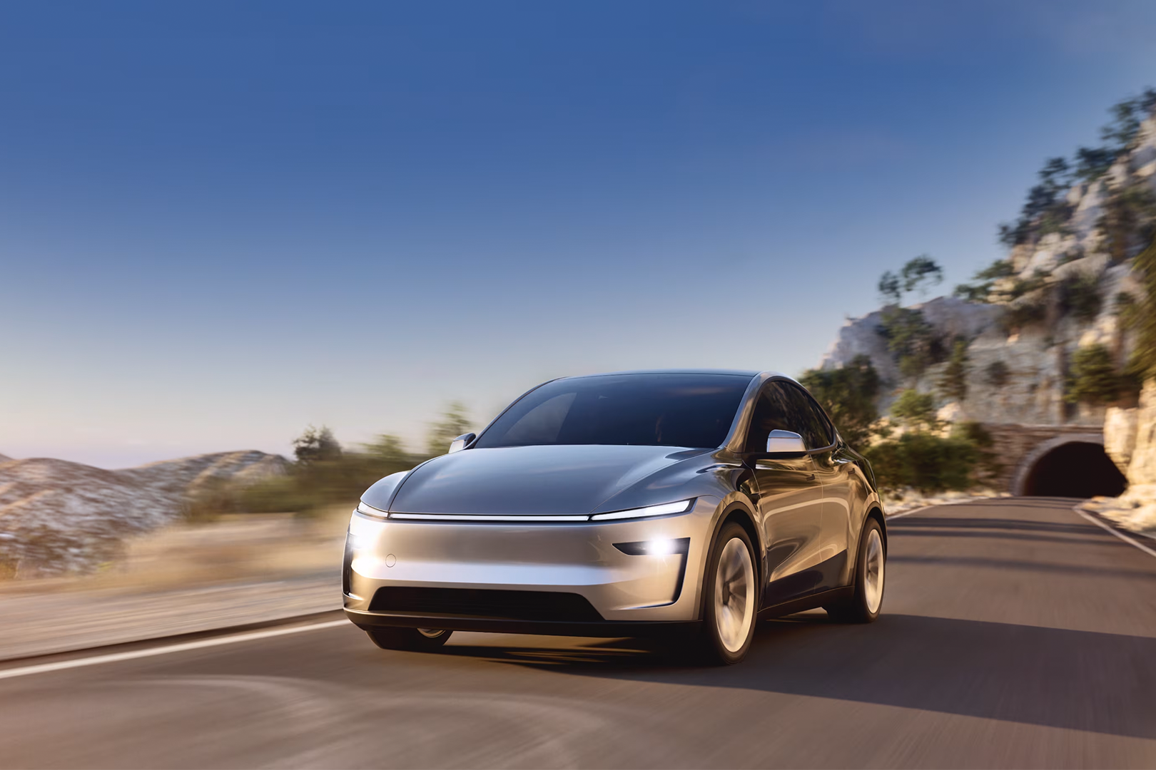 2025 Tesla Model Y facelift driving on a mountain road with a tunnel in the background.