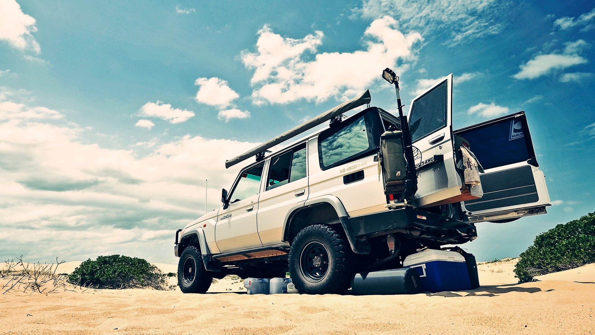 4x4 vehicle with boot open on a sandy beach, showcasing space for luggage and outdoor gear.