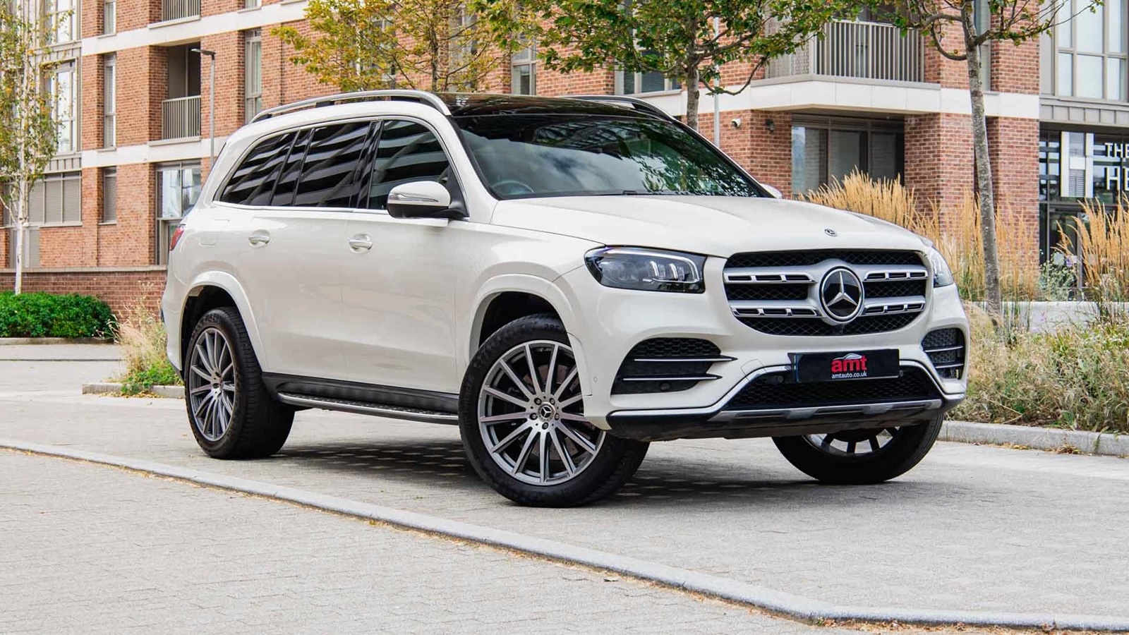 White Mercedes-Benz GLS SUV parked in front of modern brick buildings, featured on AMT Auto's Mercedes-Benz lease deals page.