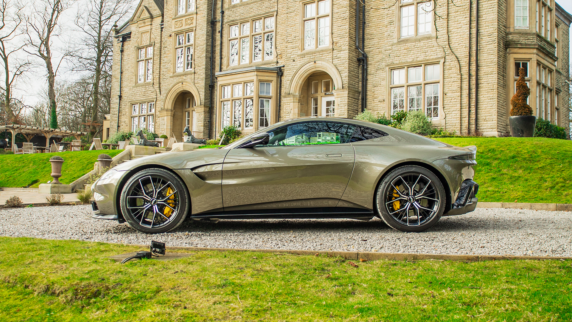 Side profile of an Aston Martin parked outside a luxury business venue, symbolising executive car leasing for companies.