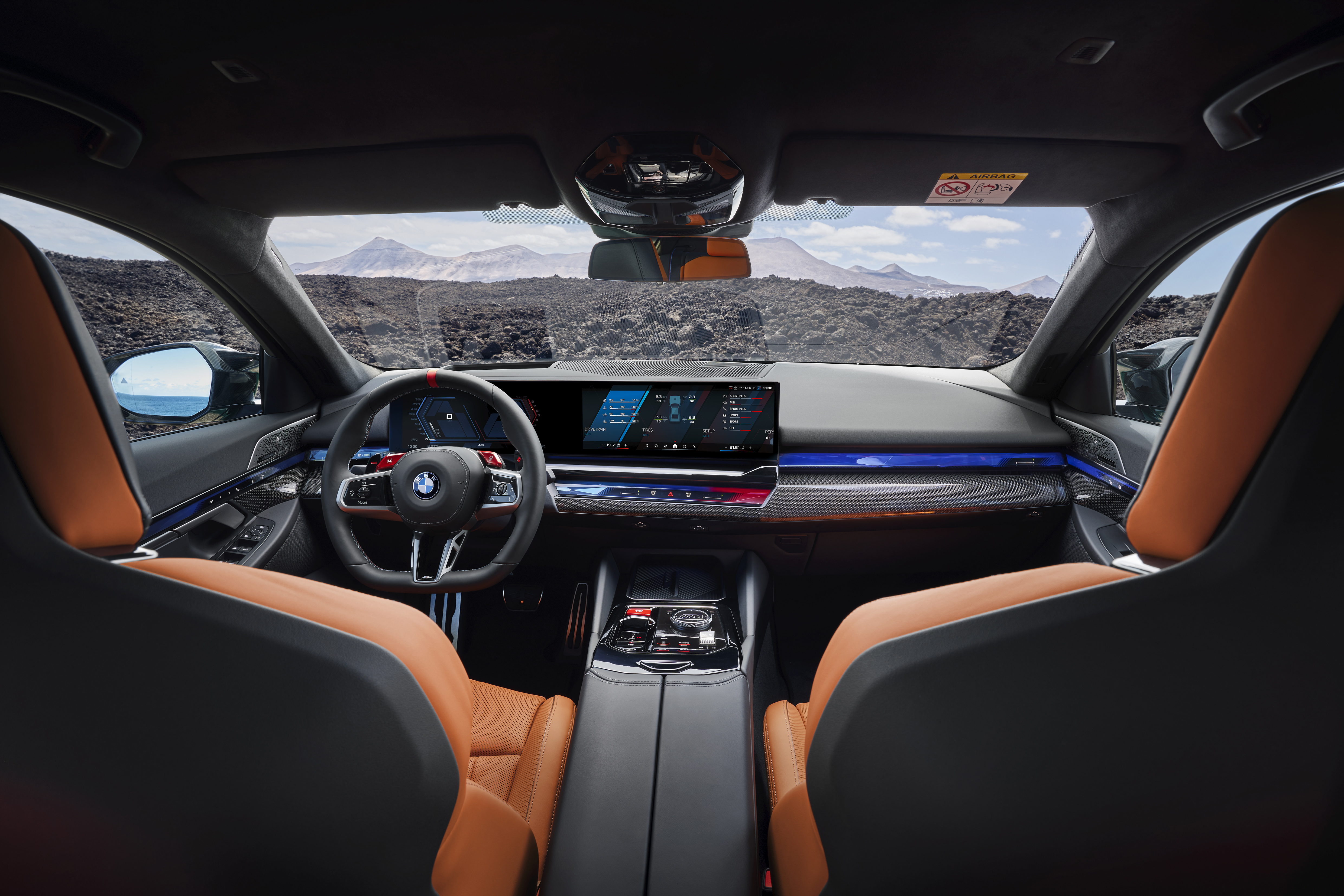 Interior view of a BMW M5, showcasing the dashboard with digital displays, leather upholstery, and steering wheel with logo.