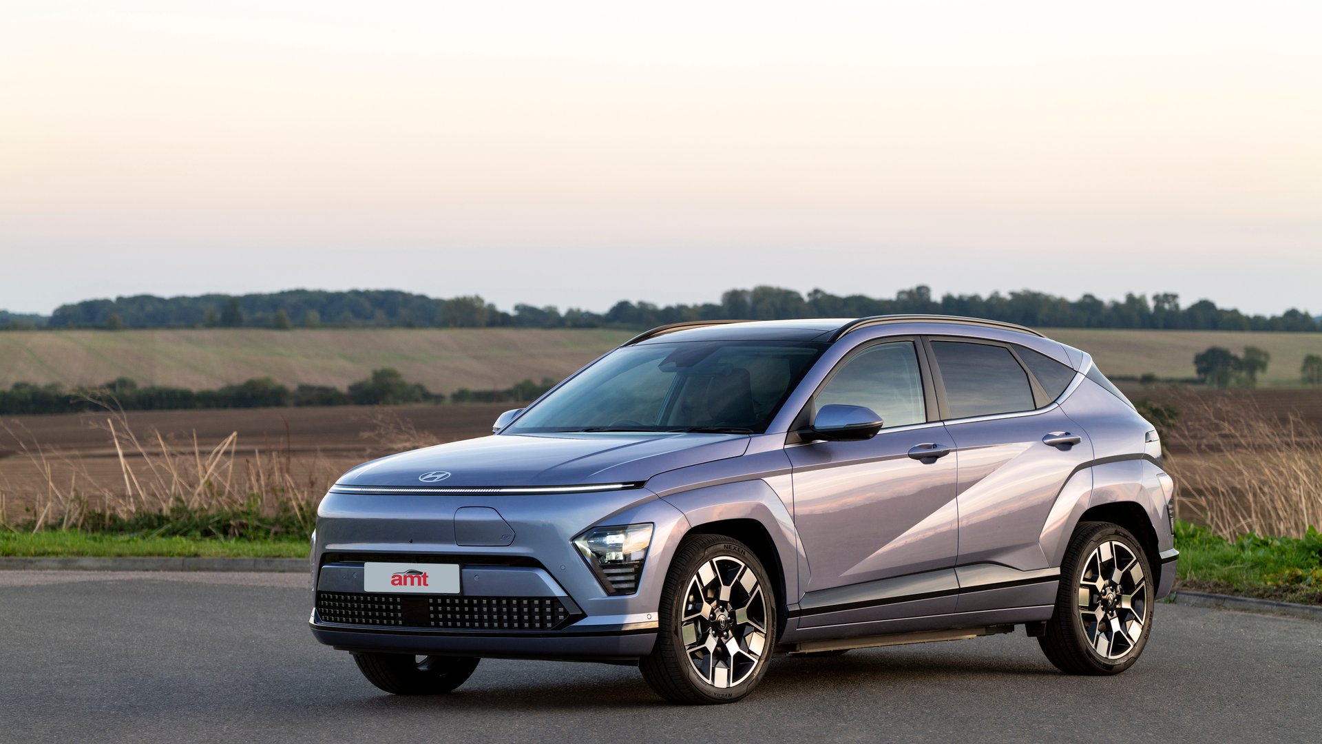 Hyundai Kona Electric in metallic blue parked on countryside road, illustrating AMT's leasing review of this efficient EV.