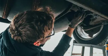 An image of a man working underneath a car