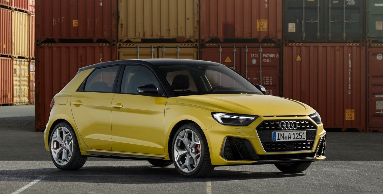 Yellow Audi A1 parked in front of shipping containers, showcasing its sporty compact design.