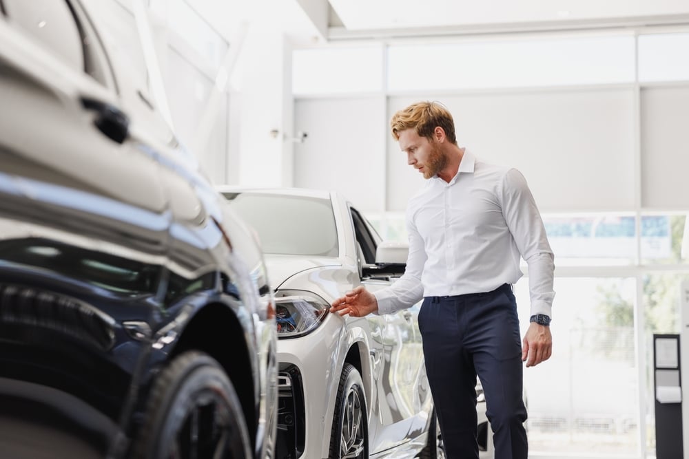 Man inspecting a white car in a bright showroom, comparing vehicle finance options.