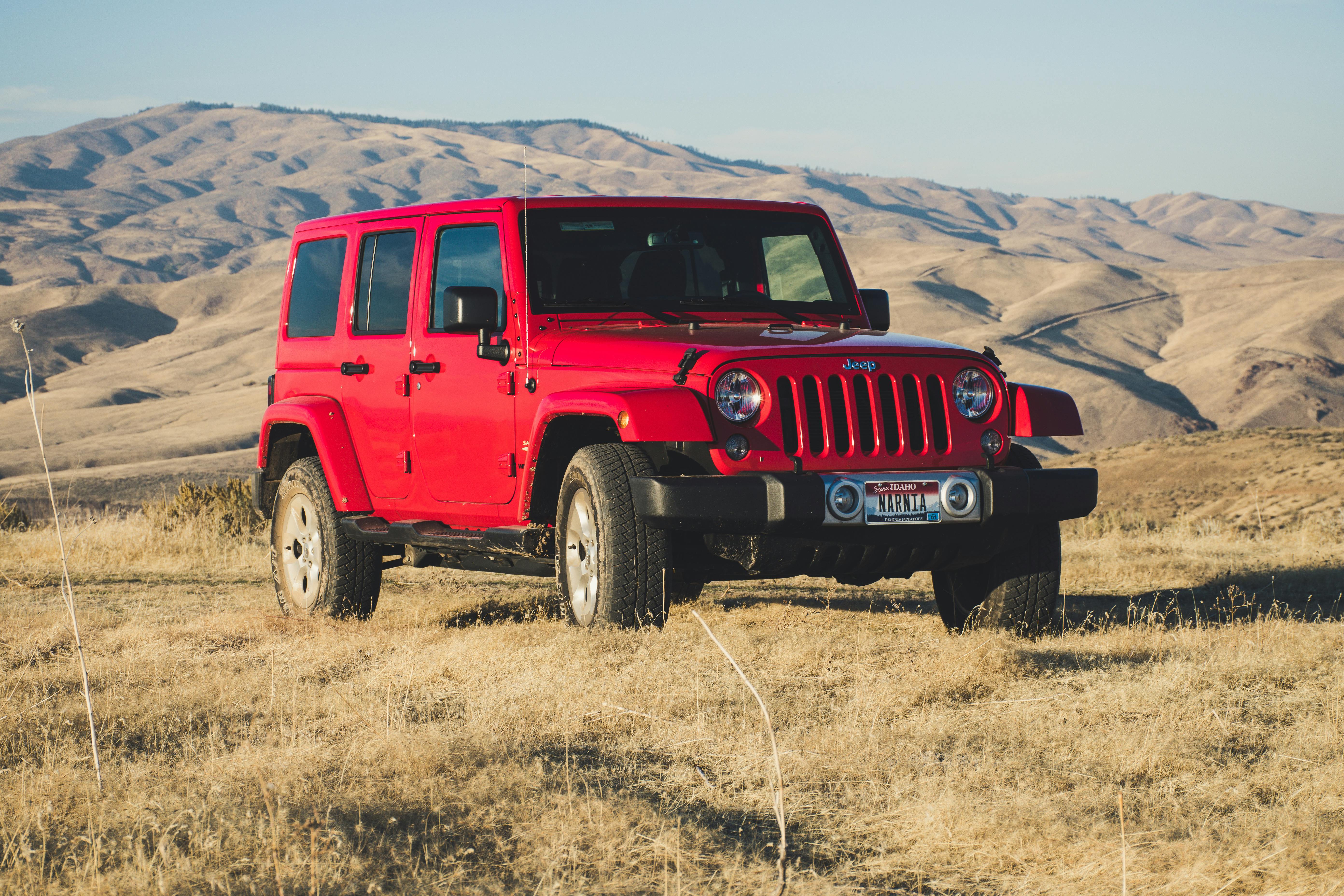 A Jeep Wrangler navigating a rocky trail, highlighting its rugged design and exceptional off-road performance. The vehicle features iconic round headlights, a seven-slot grille, and large, knobby tyres, ideal for handling rough terrain and outdoor adventures.
