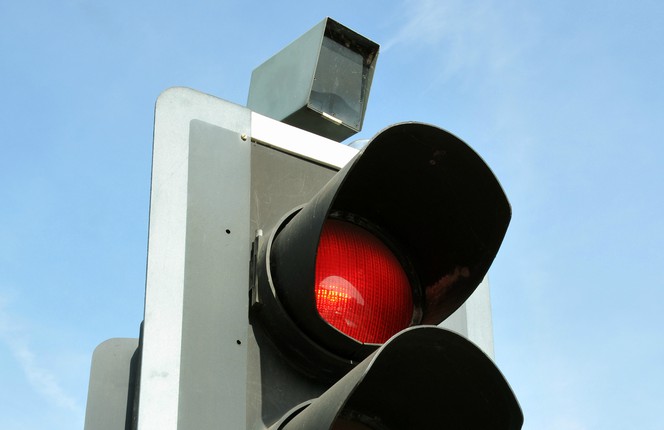An image showing a red traffic light camera on top of a standard UK traffic light