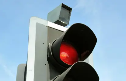 An image showing a red traffic light camera on top of a standard UK traffic light